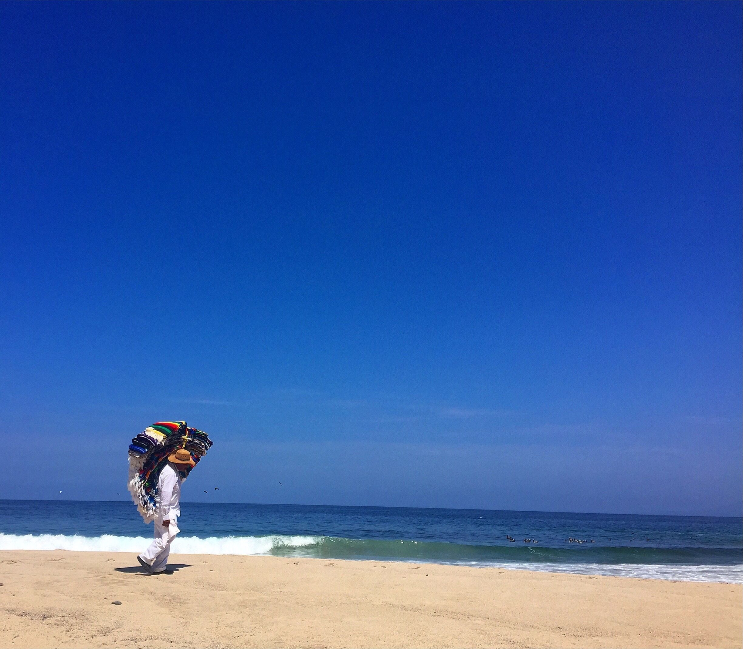 blanket vendor patiently walking the beach, hoping for a sale. 