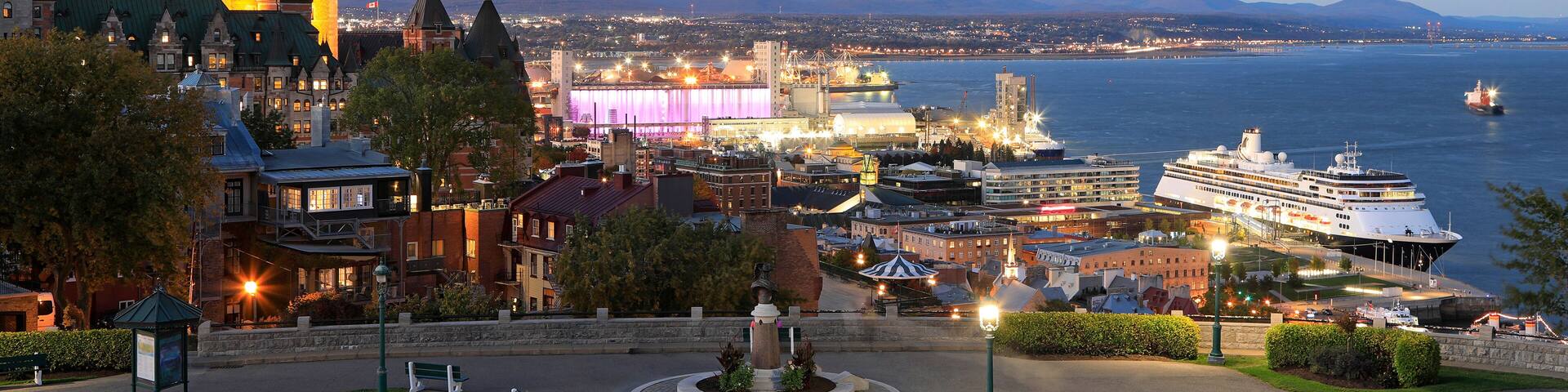 A waterfront cityscape with a historic building, a modern stadium, and a cruise ship docked.