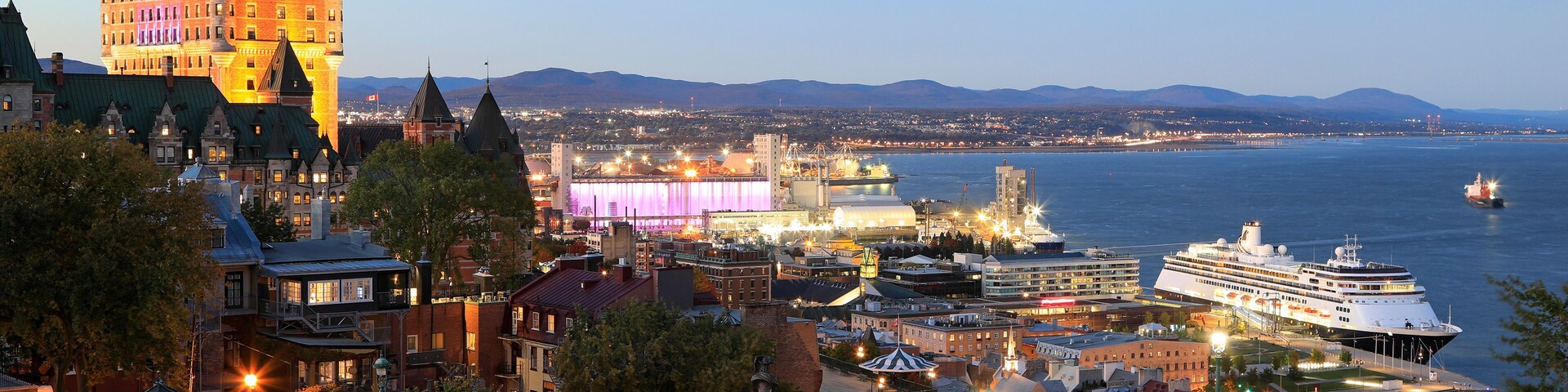 Une vue sur la ville, avec ses bâtiments historiques, un stade moderne et un navire de croisière amarré au bord de l’eau.