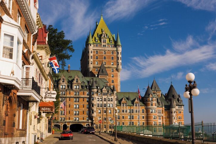 A historic building with a green spire, a hotel sign, and flags.