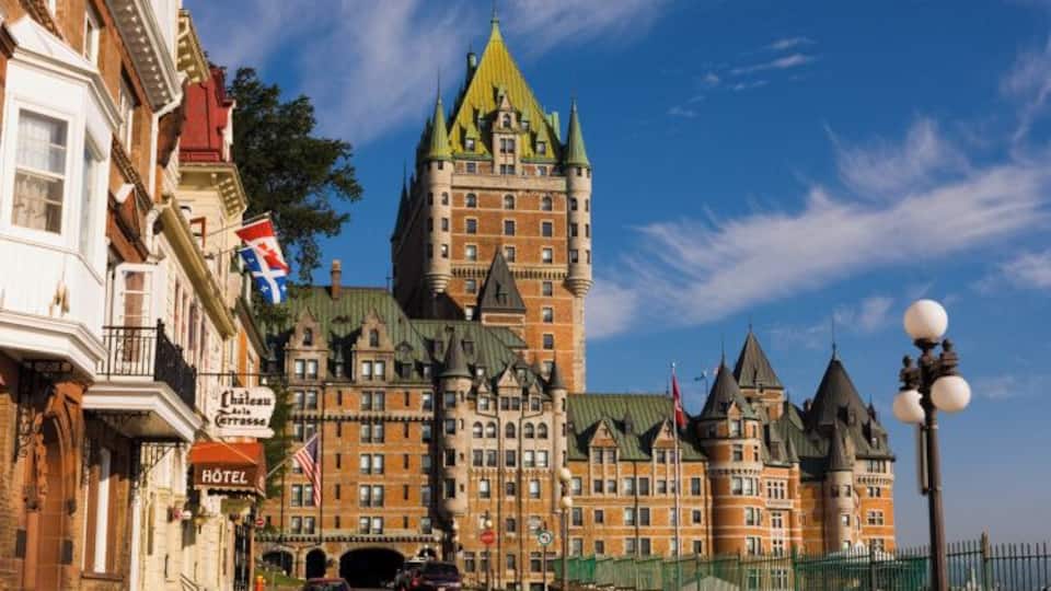 A historic building with a green spire, a hotel sign, and flags.