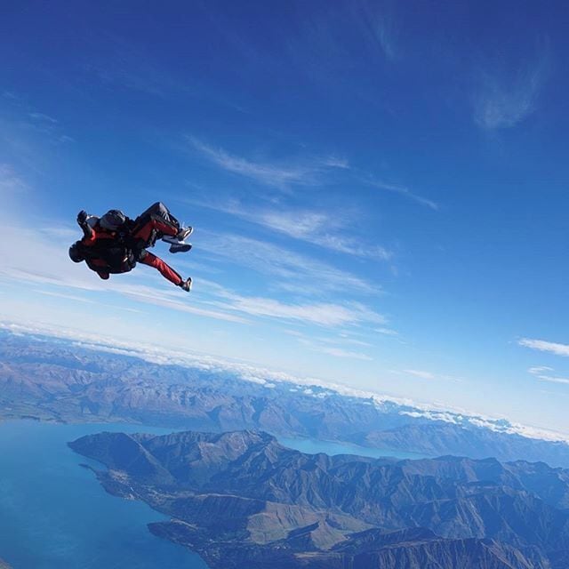A person skydiving over a mountainous landscape with a lake below.