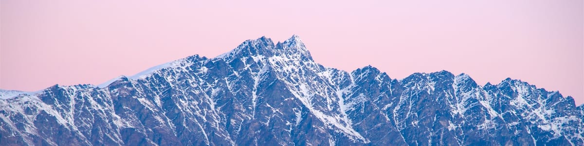 A mountain range with snow-capped peaks and rolling hills in the foreground.