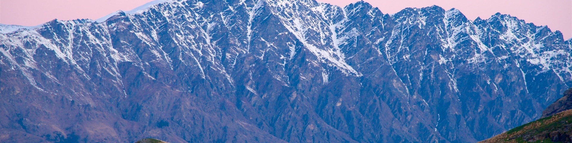 Una cordillera con picos nevados y colinas onduladas en primer plano.