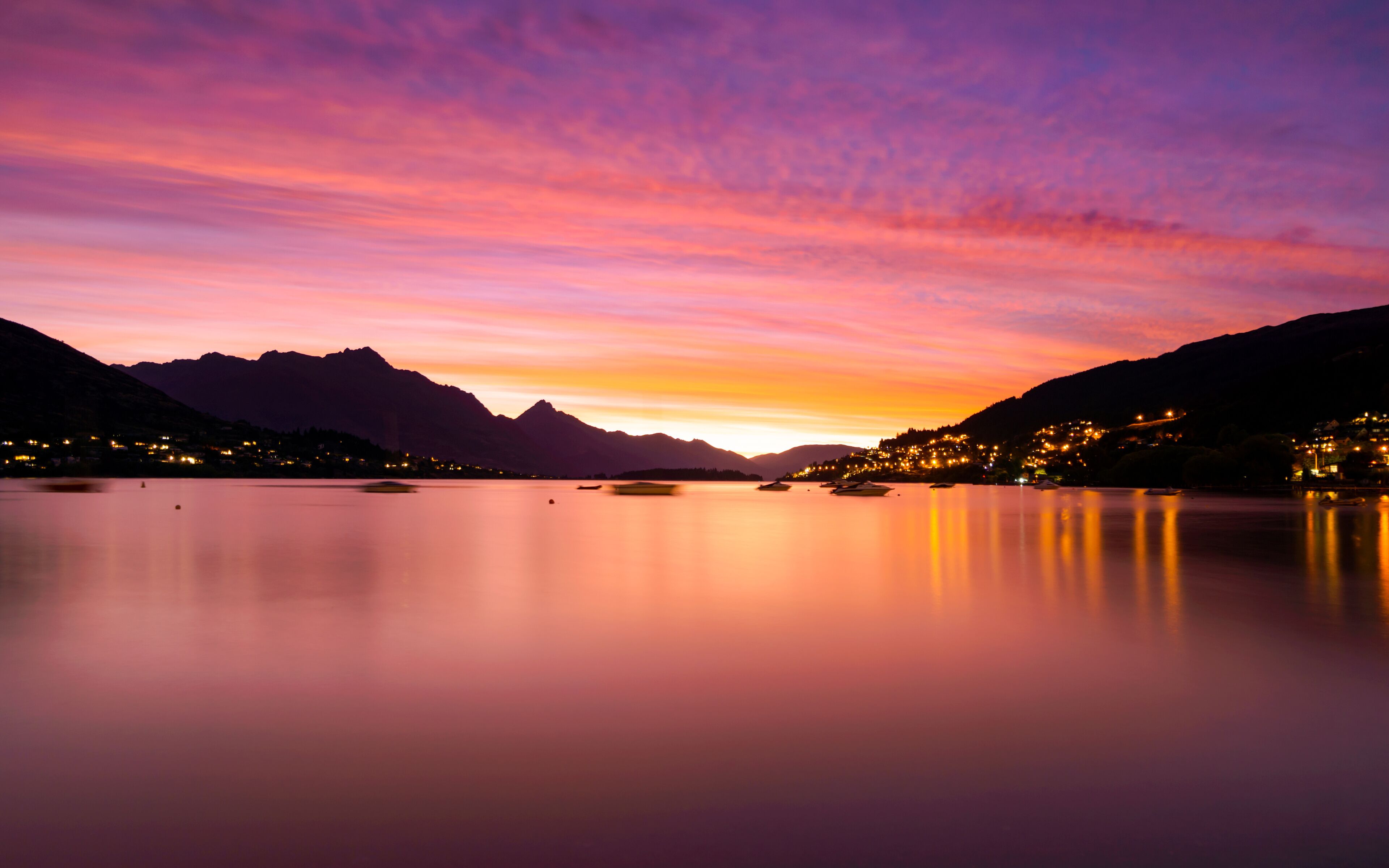 Un lago tranquilo al atardecer con montañas al fondo y un pueblo en la orilla opuesta.