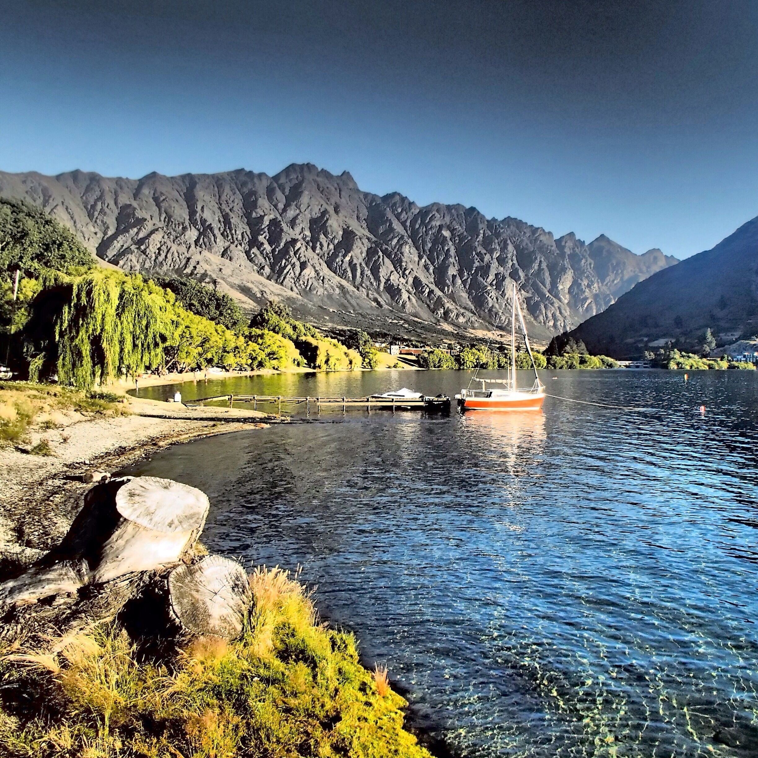 A river with a boat, mountains in the background, and greenery along the riverbank.