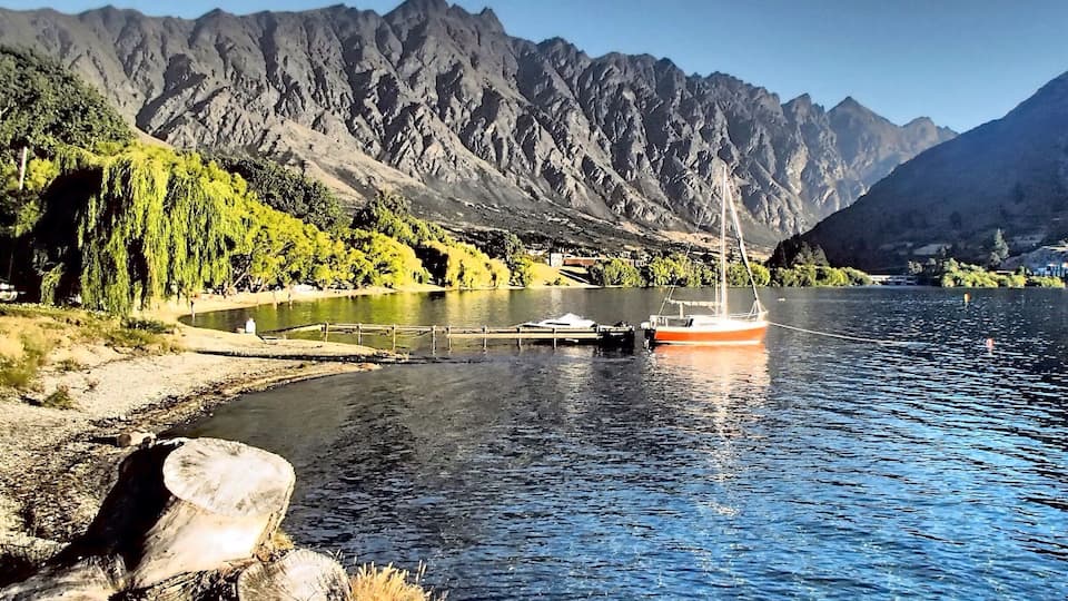 A river with a boat, mountains in the background, and greenery along the riverbank.