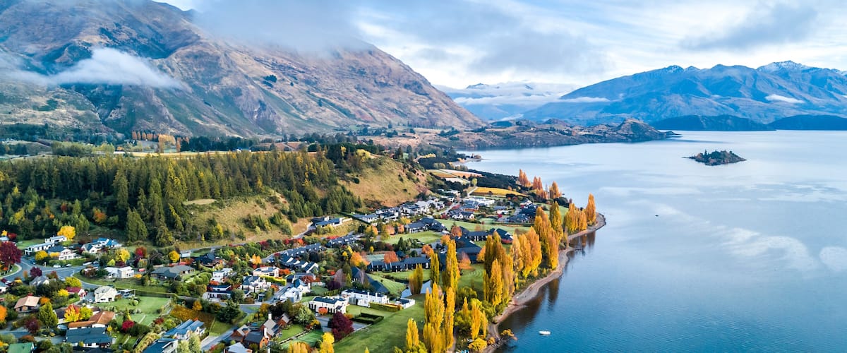 A mountainous landscape with a lake, a village, and autumn-colored trees.