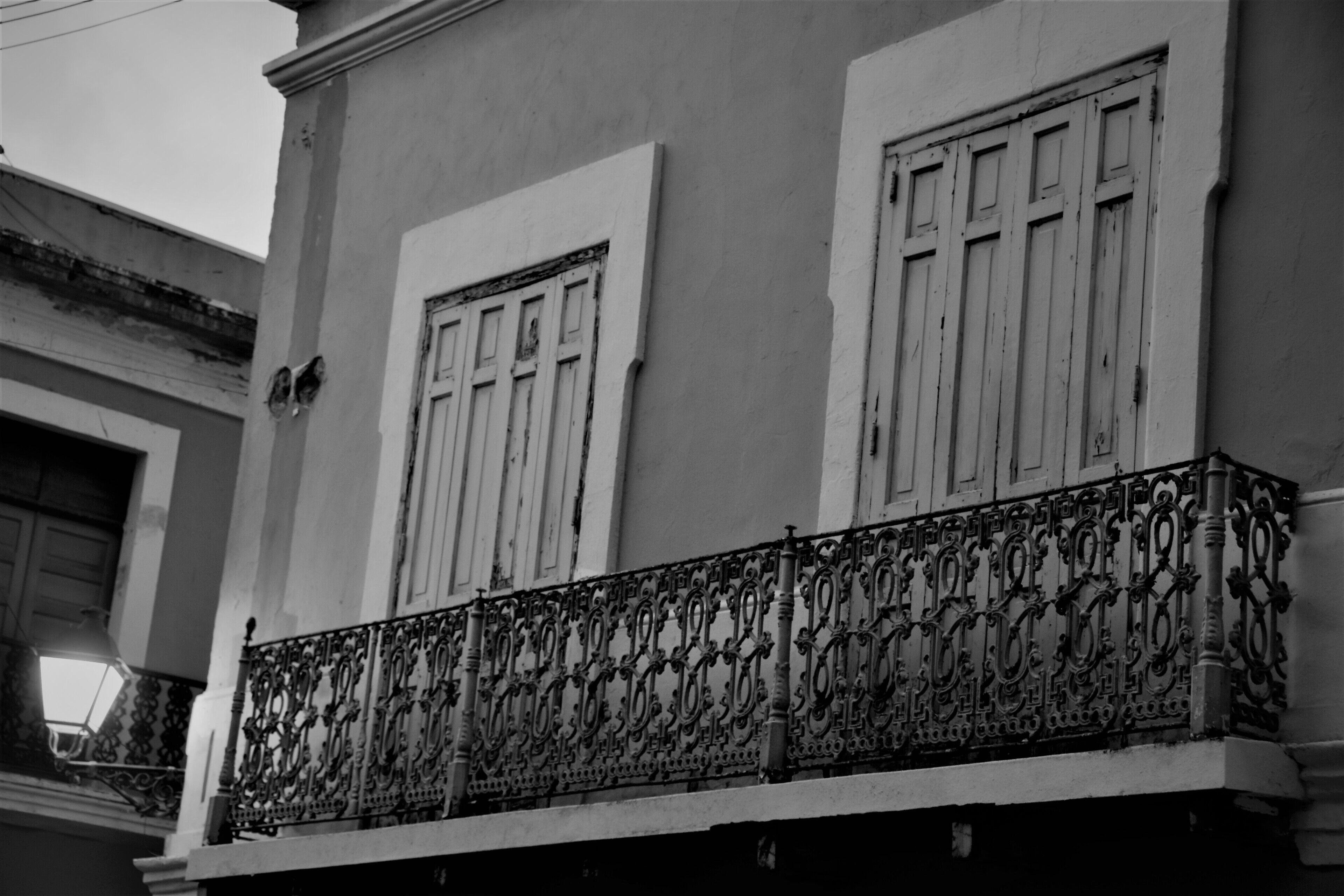 A building with ornate wrought iron balcony railings and white-framed windows.