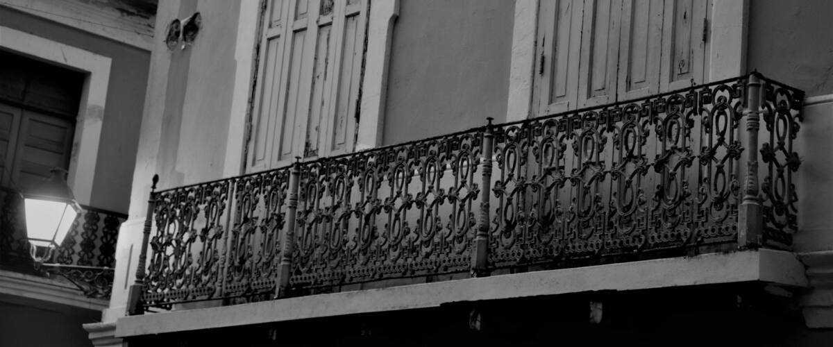 A building with ornate wrought iron balcony railings and white-framed windows.
