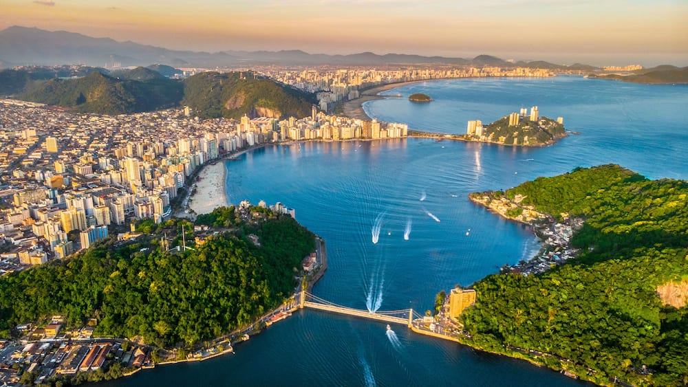 A coastal city with a bridge, dense urban area, and surrounding hills.