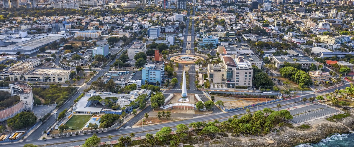 An aerial view of a coastal city with a prominent central monument, dense urban buildings, and a rocky shoreline.