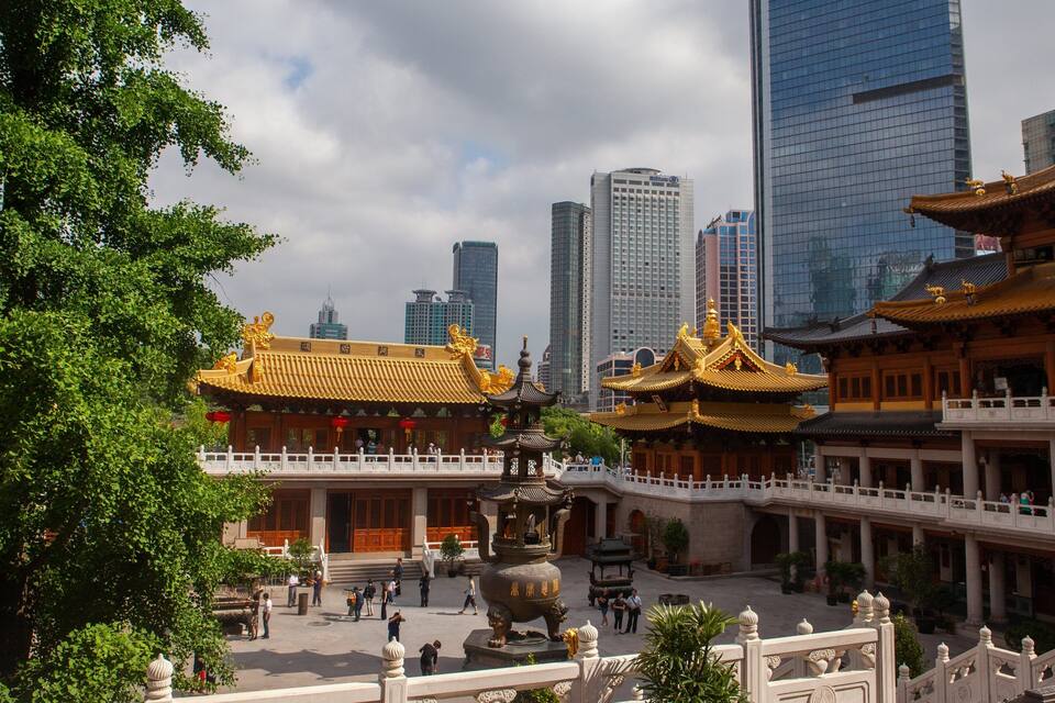 A traditional Chinese courtyard with ornate buildings and a modern cityscape in the background.