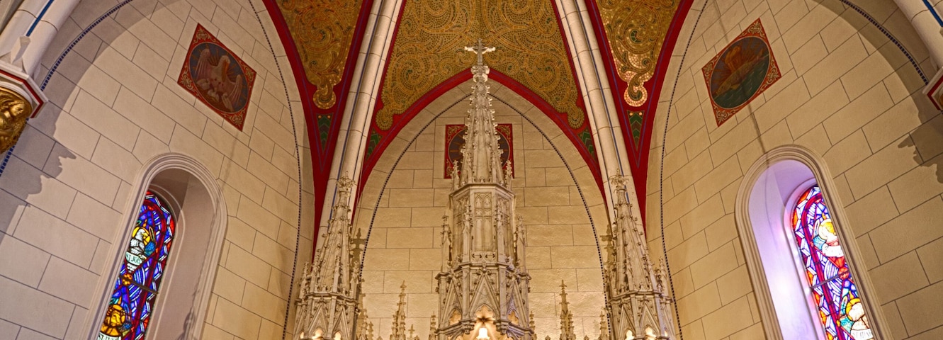 Interior de igreja ornamentado, com altar alto, vitrais e detalhada arte no teto.