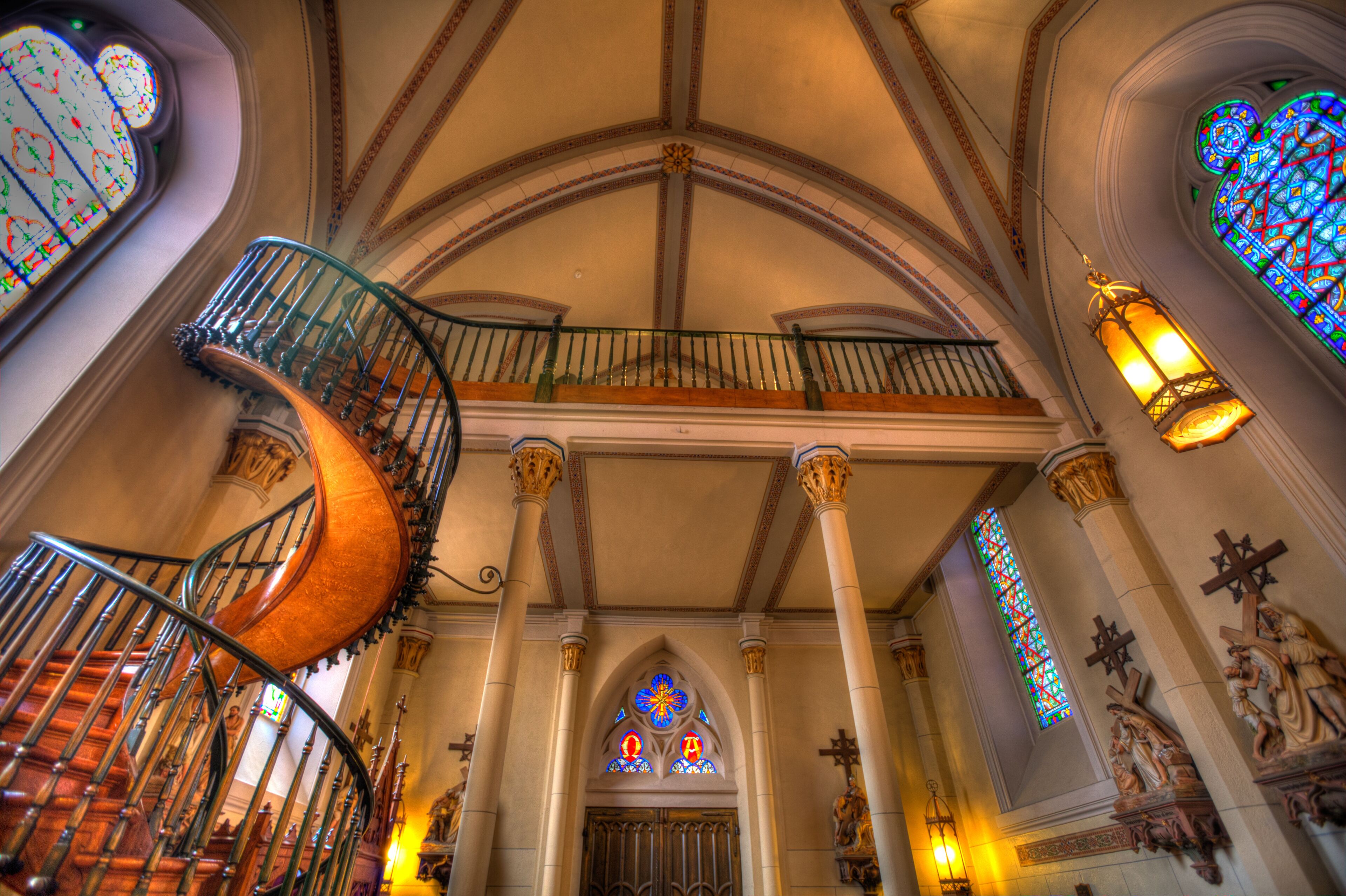 A spiral staircase with ornate railings, a vaulted ceiling, and stained glass windows.