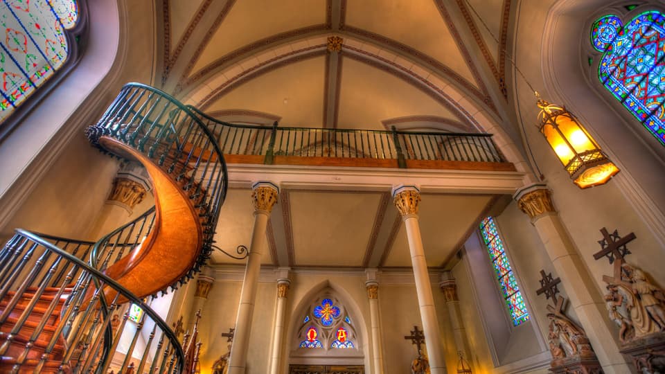 A spiral staircase with ornate railings, a vaulted ceiling, and stained glass windows.