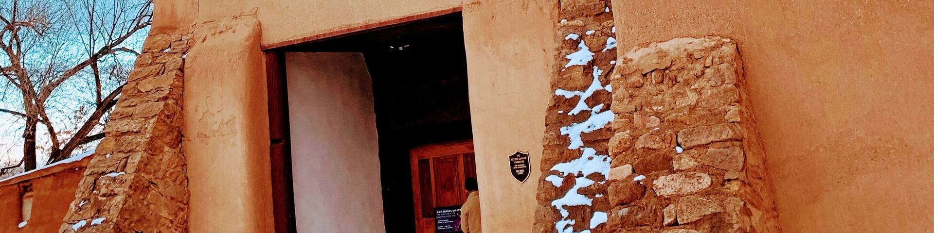 Una iglesia con una cruz en la parte superior, una campana y el suelo cubierto de nieve.