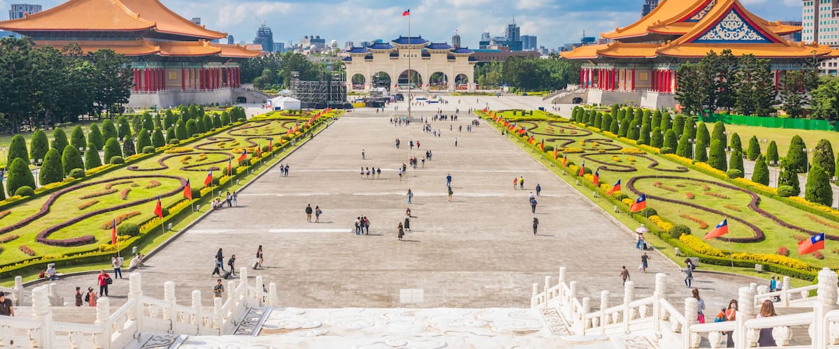 A large open plaza with traditional architecture, a central archway, and symmetrical gardens.