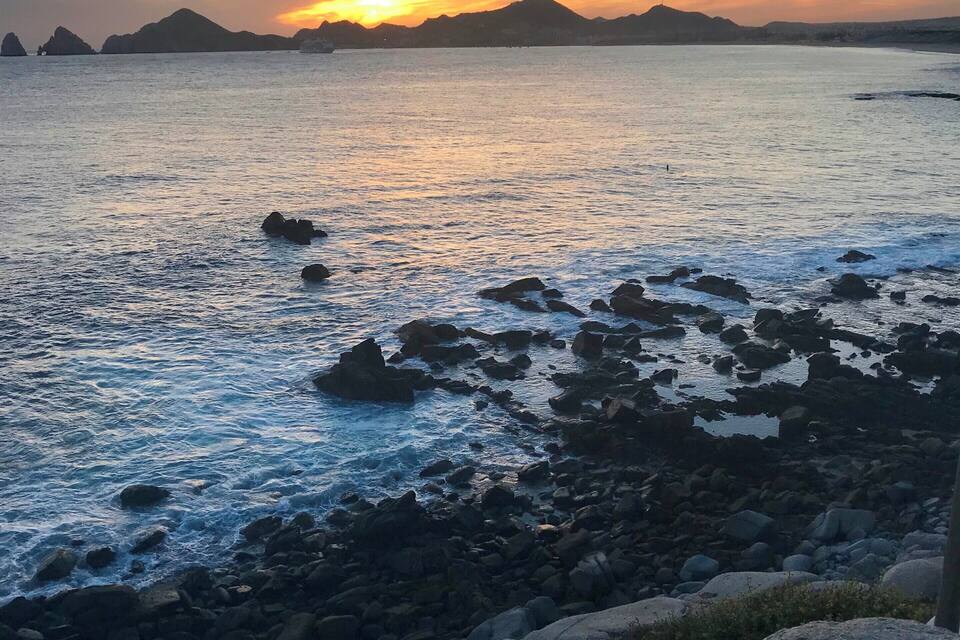 Un coucher de soleil sur la côte, avec des rivages rocheux et des montagnes lointaines.