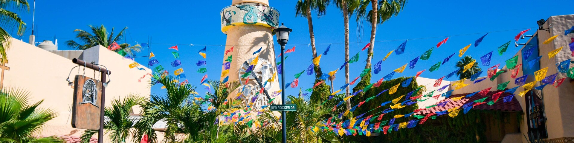 Una plaza con un edificio histórico, palmeras y banderas coloridas.