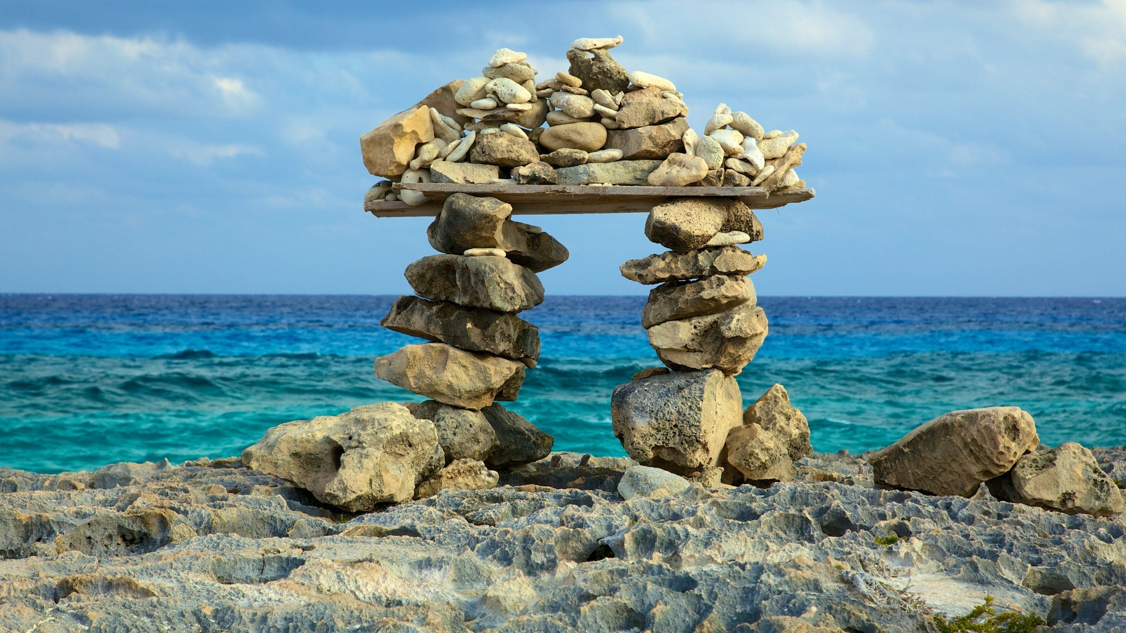 A stone structure with a shelf on top, surrounded by a rocky shoreline and the ocean.