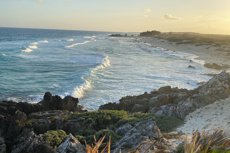 A coastal landscape with rocky outcrops, a sandy beach, and the ocean.