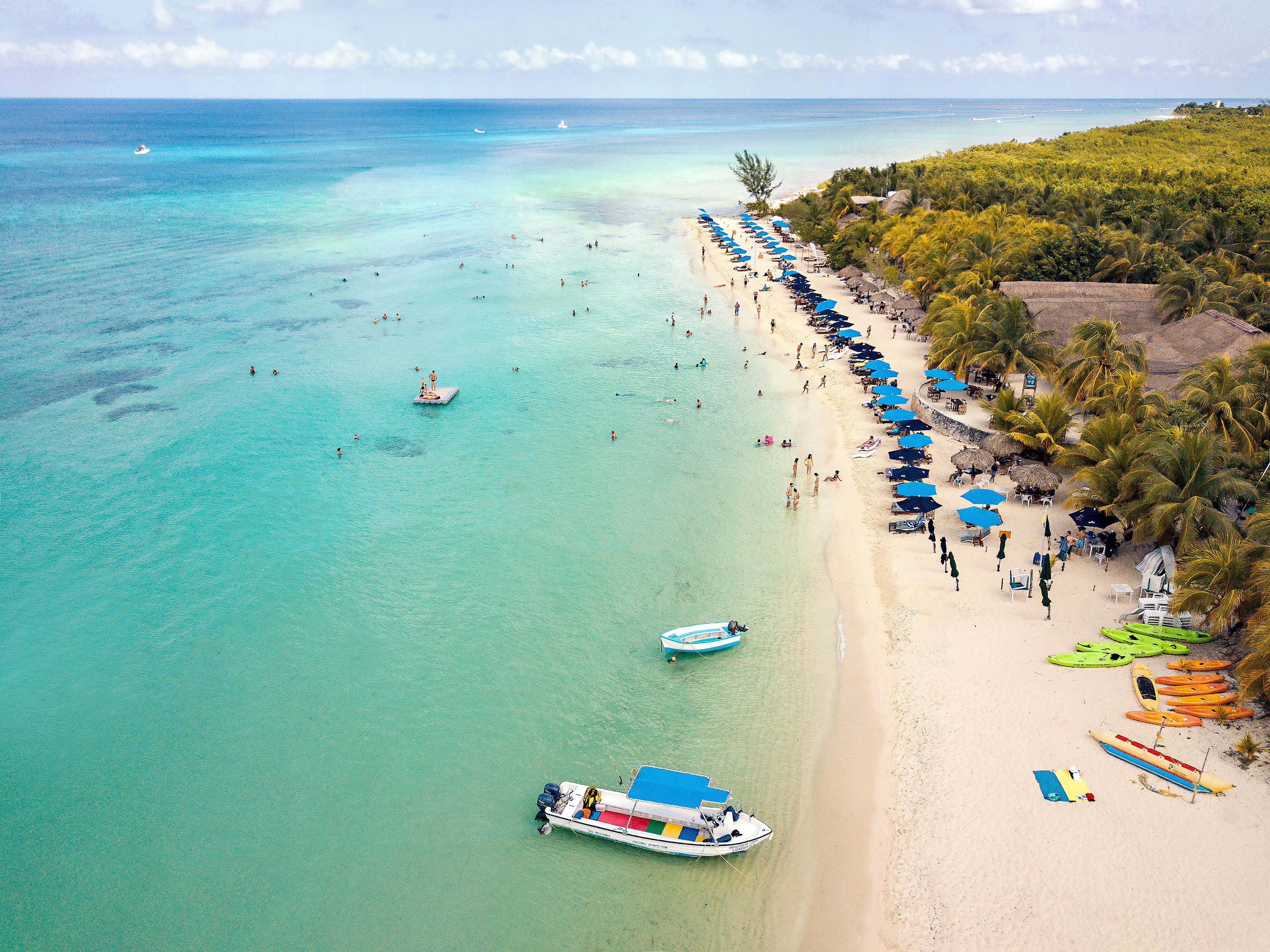 Uma praia tropical com águas turquesa cristalinas, uma fileira de guarda-sóis e um barco ancorado perto da costa.