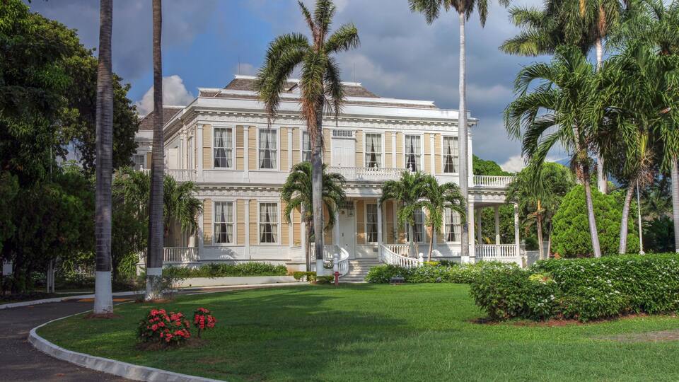 A large white building with columns, surrounded by palm trees and well-maintained lawns.