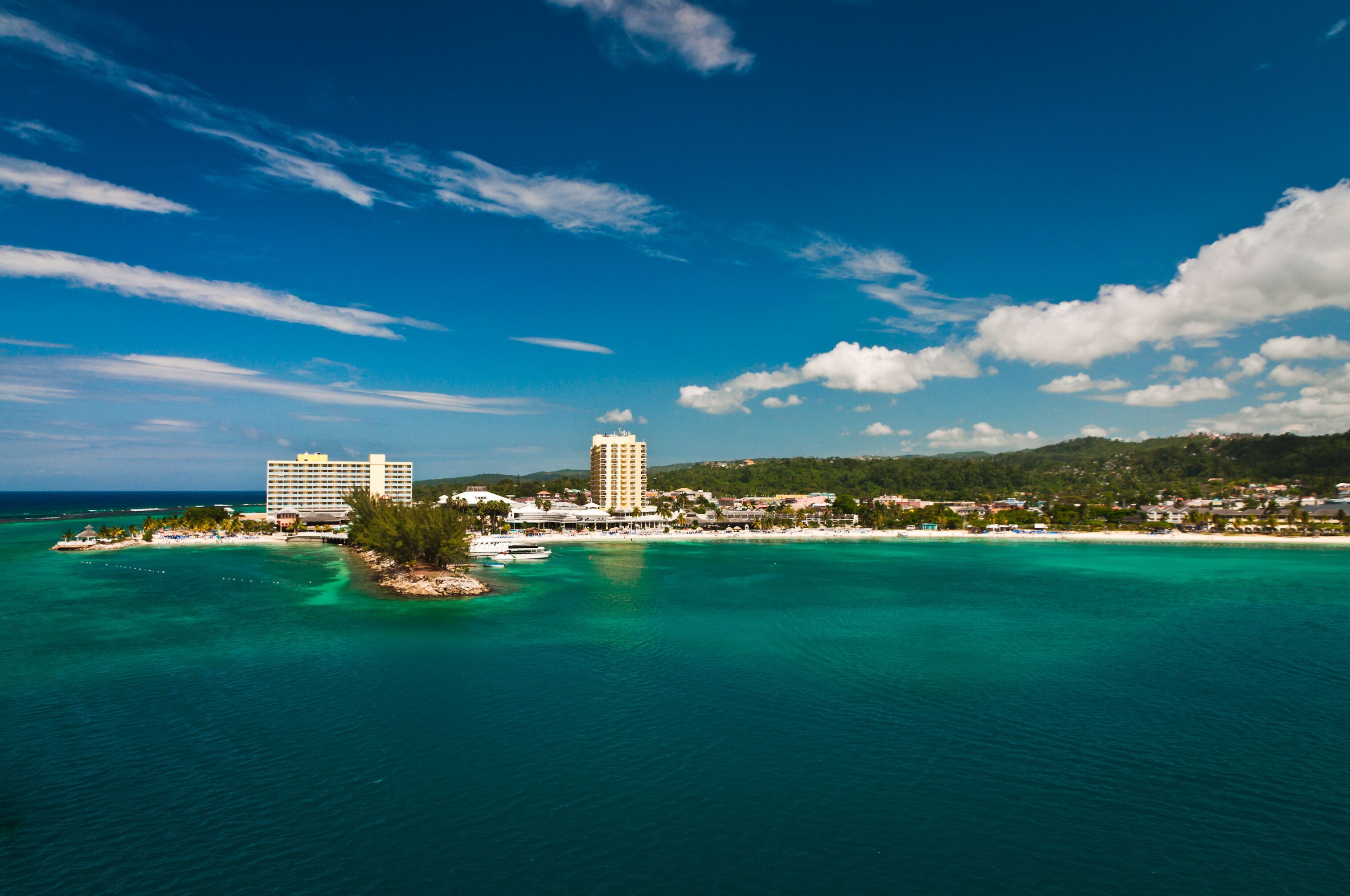 A coastal town with a clear blue sky, turquoise waters, and two prominent hotels.