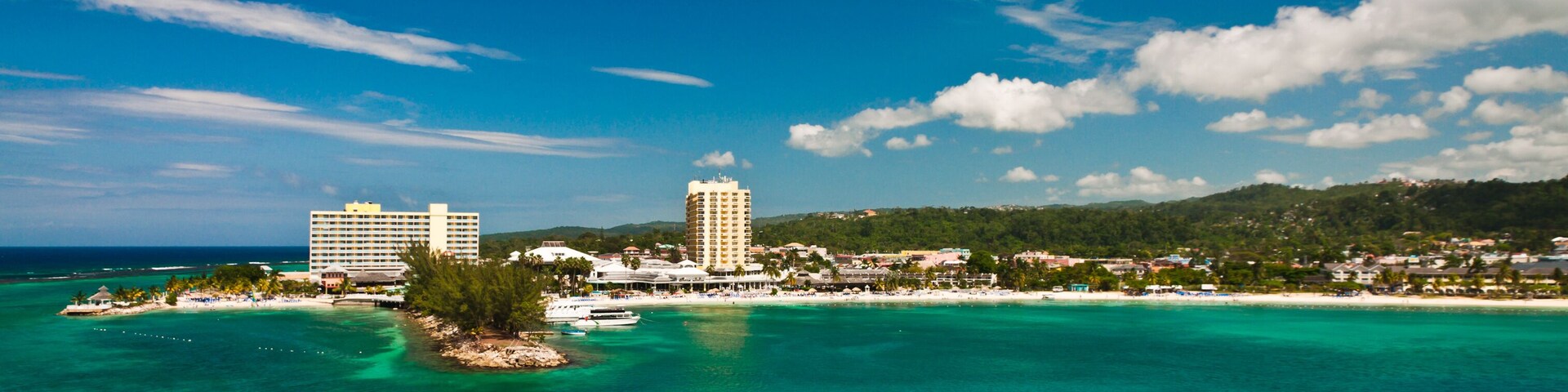 A coastal town with a clear blue sky, turquoise waters, and two prominent hotels.