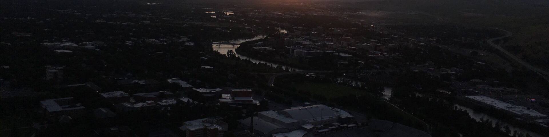 A sunset over a valley with a river, buildings, and mountains in the background.