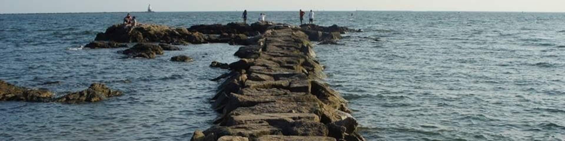 A rocky breakwater extending into the sea with people standing on it.