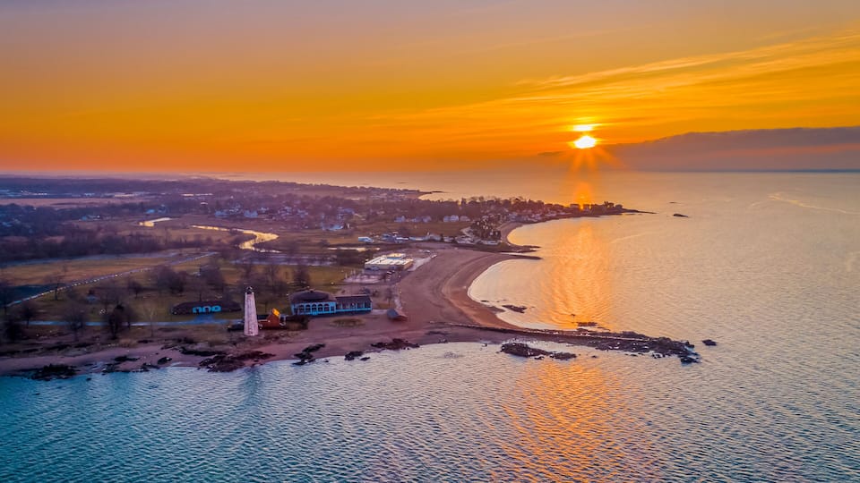 A coastal sunset with a lighthouse, beach, and town in the background.