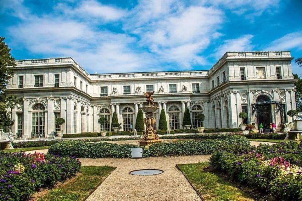 A classical building with a symmetrical facade, a central fountain, and manicured gardens.