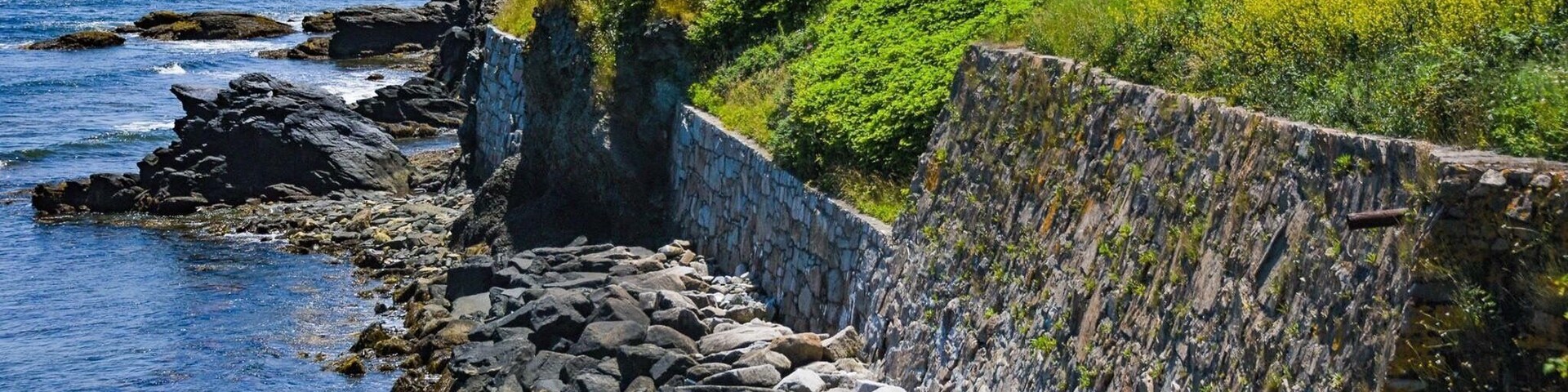 Costa rocosa con un muro de piedra y una colina cubierta de hierba.