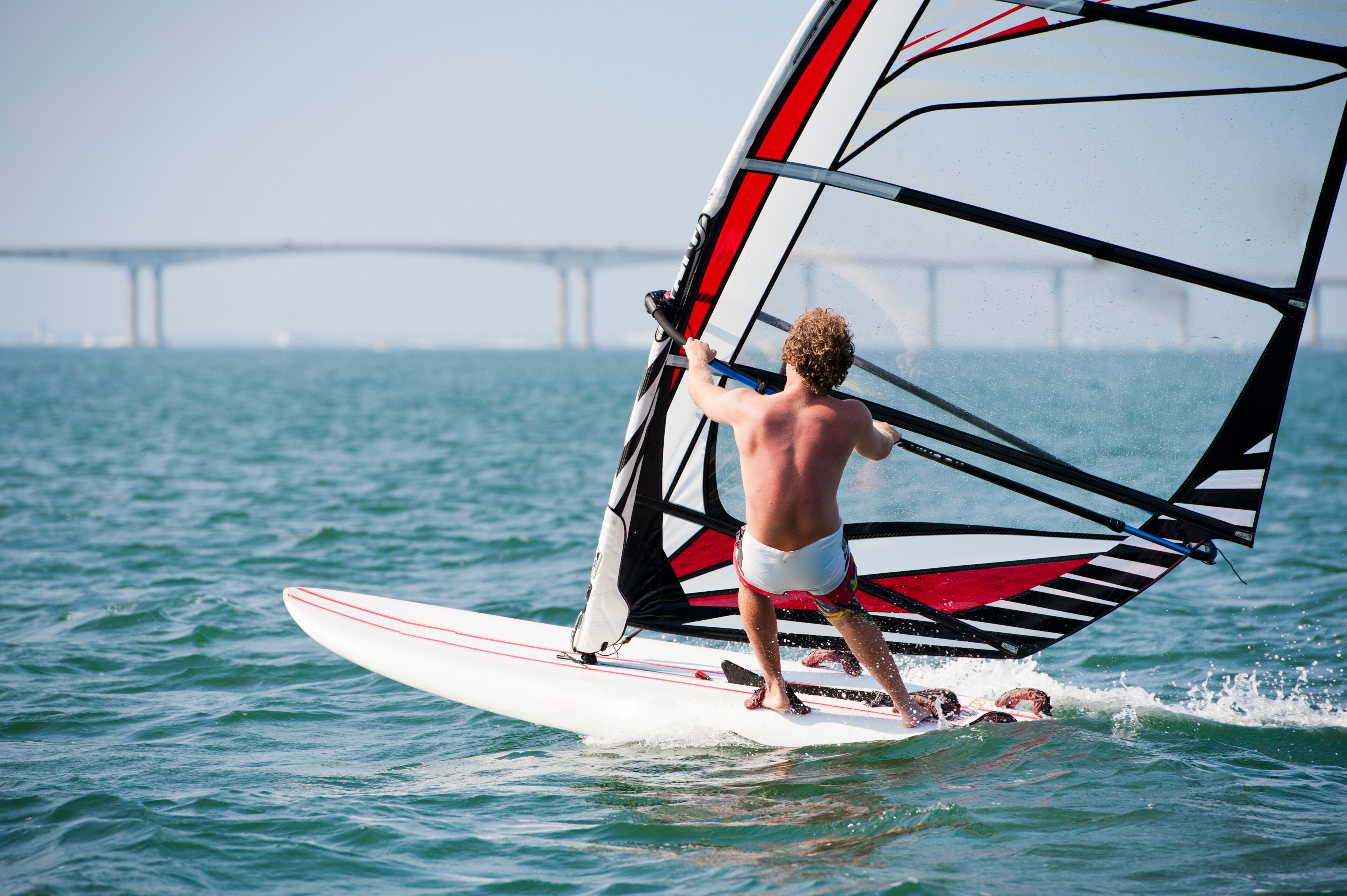 A person windsurfing on a body of water with a bridge in the background.