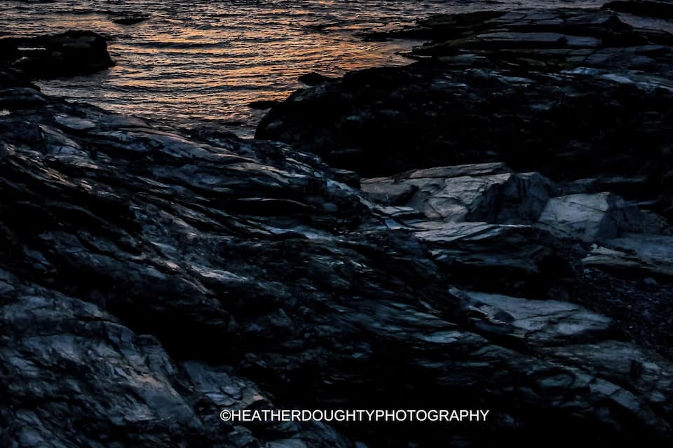 Un atardecer sobre una costa rocosa con agua tranquila que refleja el cielo.