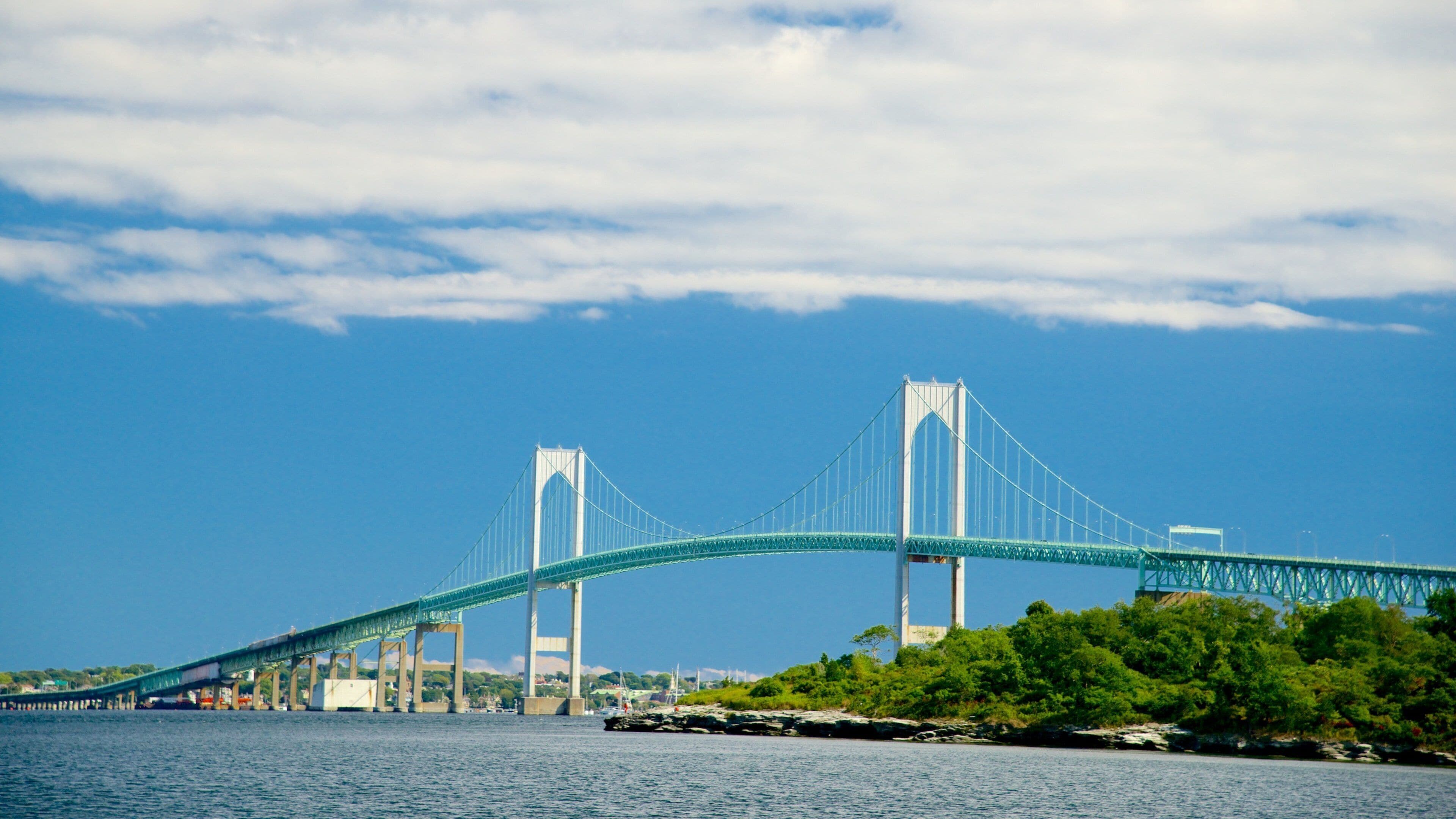 Un grand pont suspendu enjambant une étendue d’eau, avec une rive rocheuse et une végétation luxuriante au premier plan.