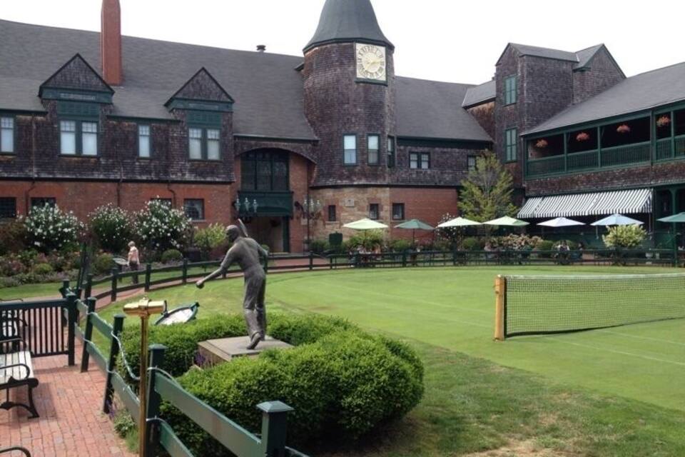 A courtyard with a tennis court, a statue, and a building with a clock tower.