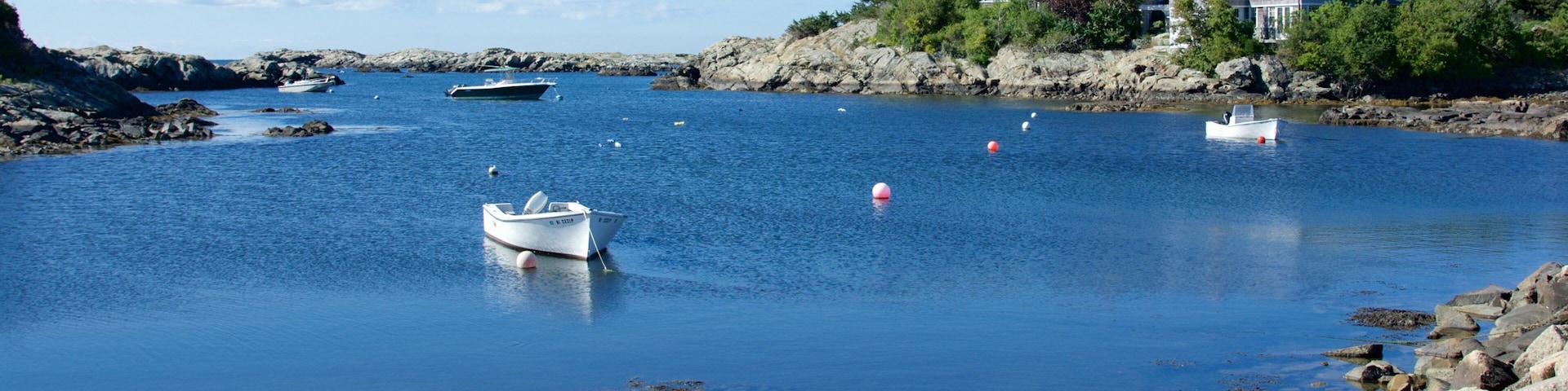 Una bahía tranquila con barcos, costa rocosa y una casa grande en un acantilado.