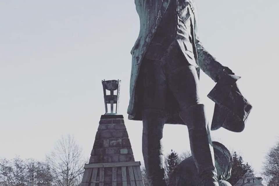 A statue of a historical figure with a raised arm, a pedestal, and a small monument with a chair on top.