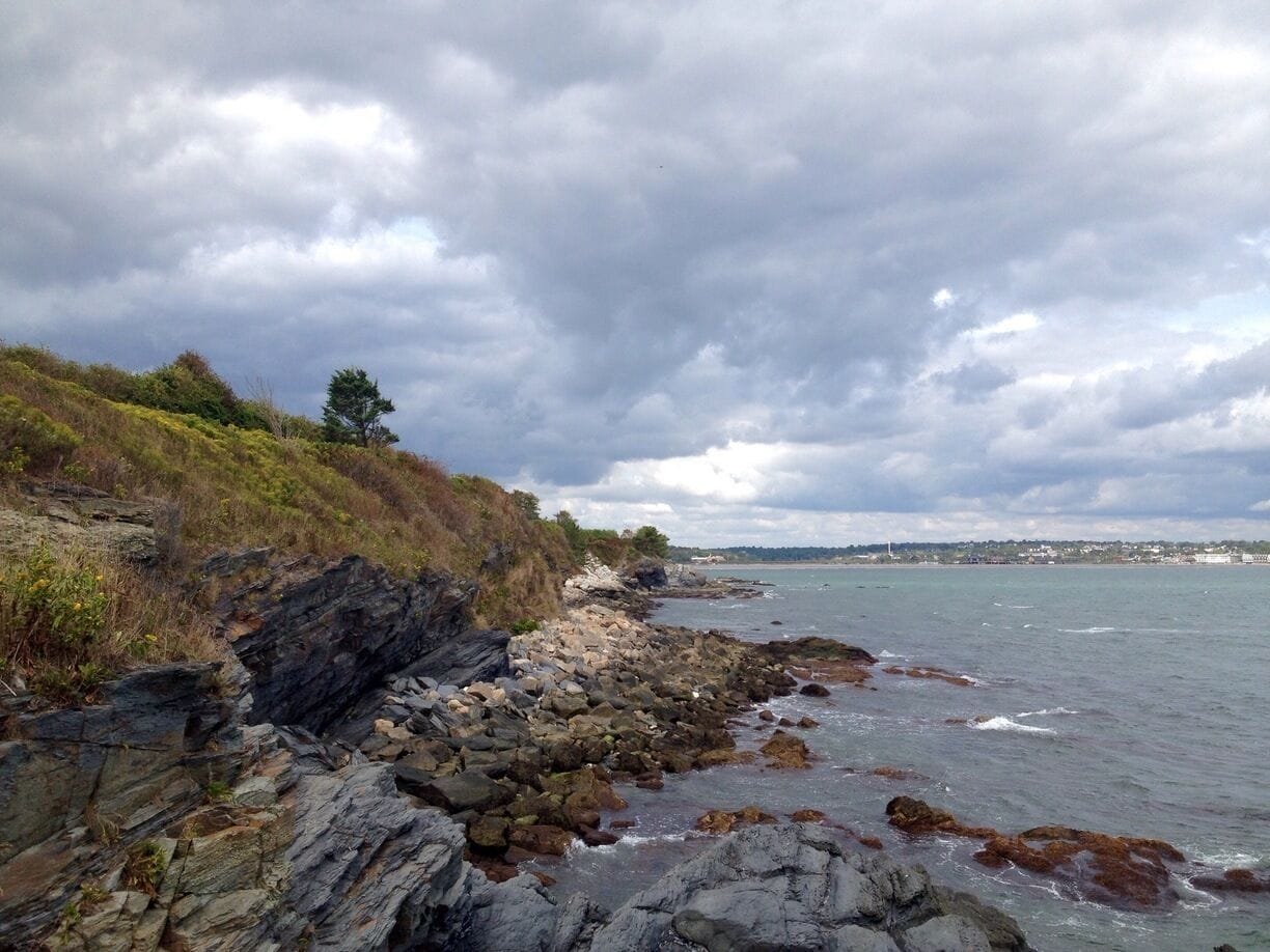 A rocky shoreline with waves crashing against the rocks under a cloudy sky.