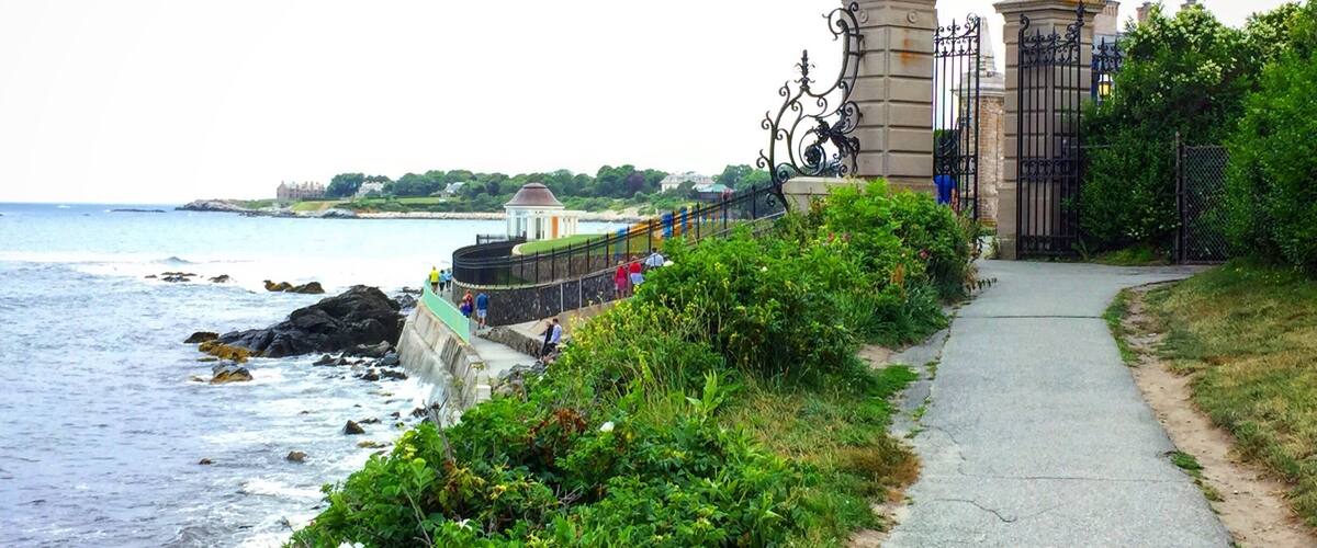 A coastal walkway with a stone wall, a gate, and a view of the sea.