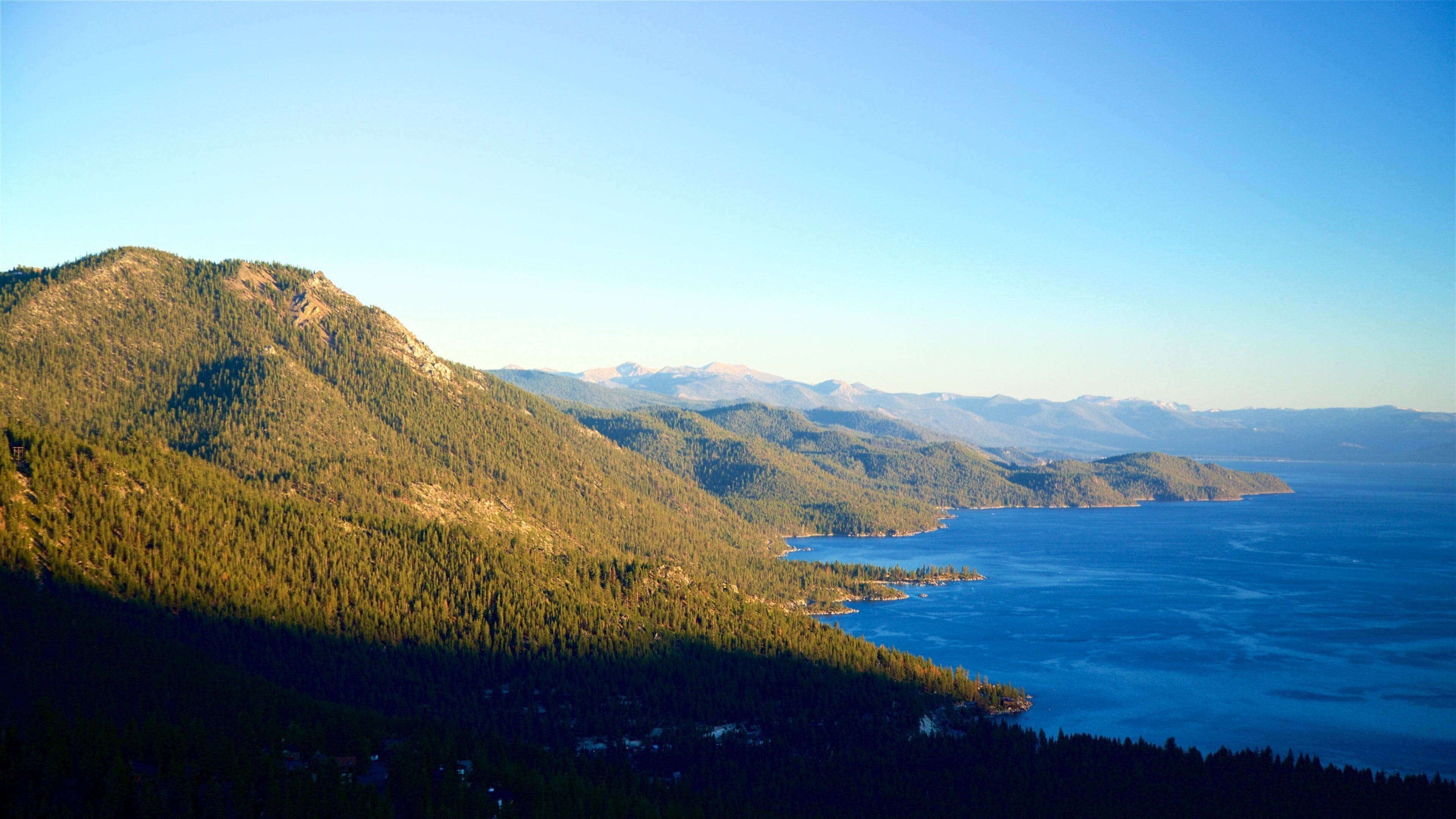 A coastal mountain range with a clear view of the ocean and distant snow-capped mountains.