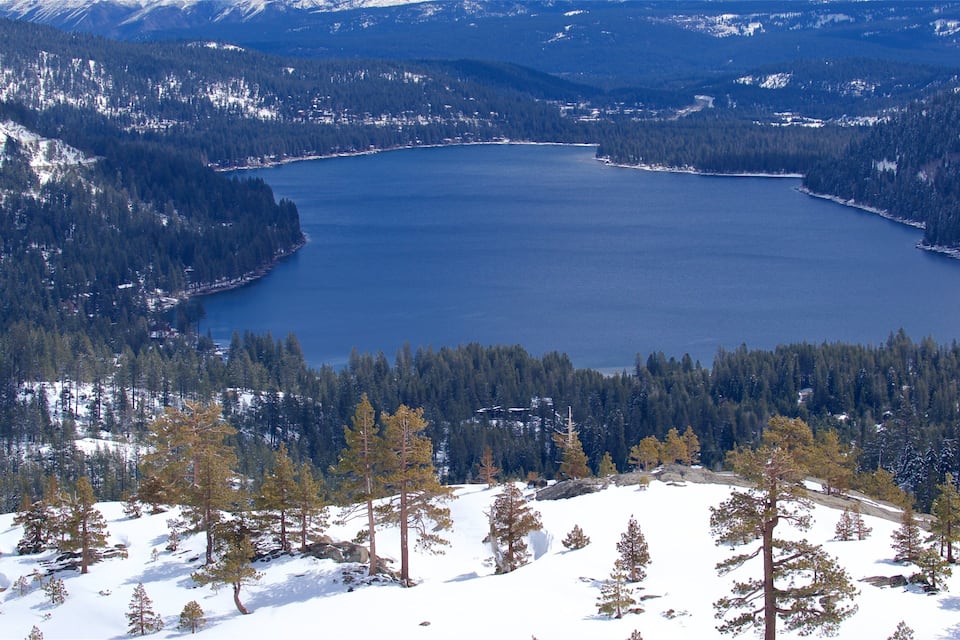 A large lake surrounded by dense forests and snow-covered mountains.