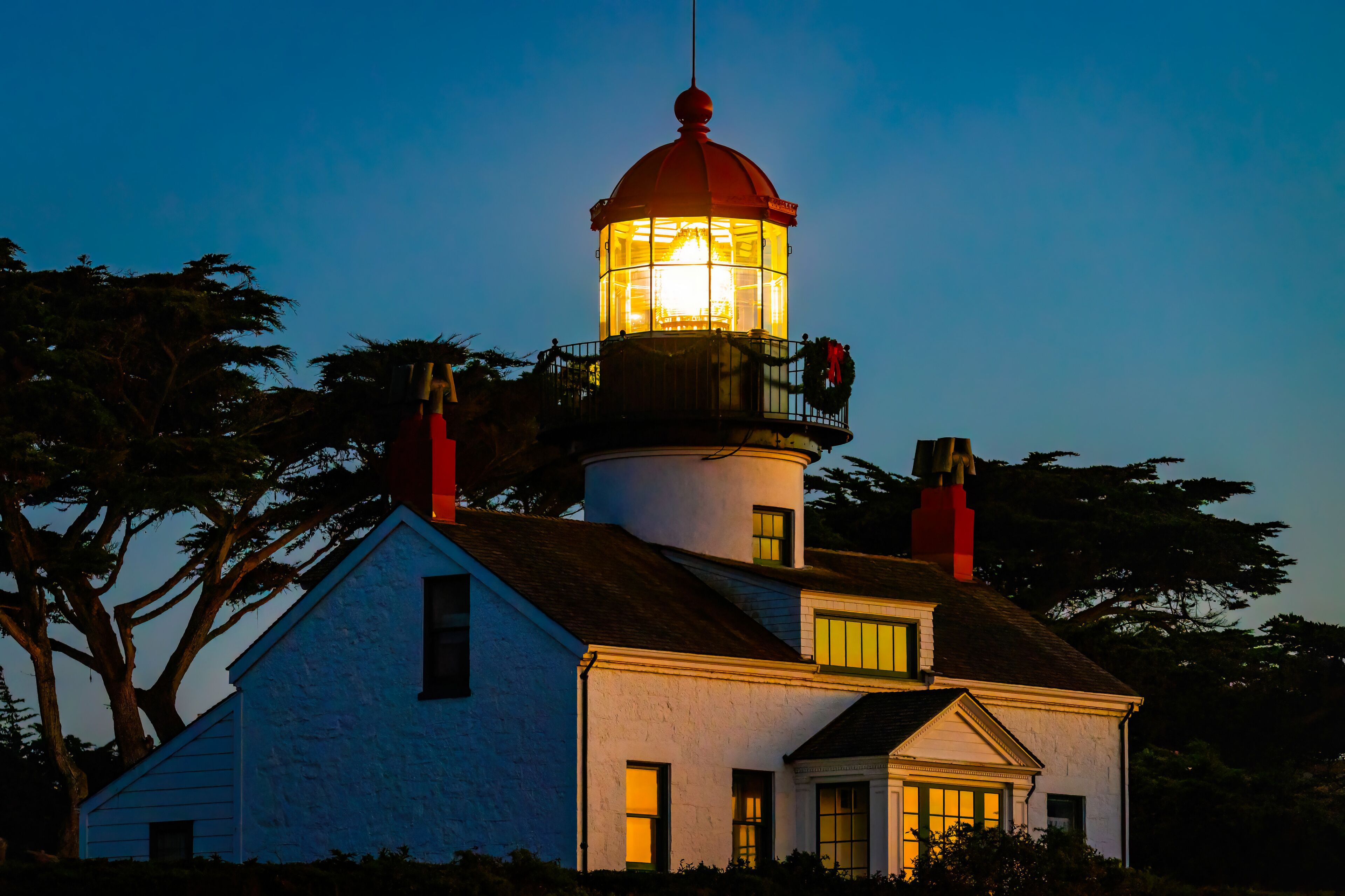 A lighthouse with a red top, white walls, and a balcony with a wreath.