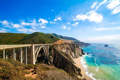 A coastal bridge with a mountainous backdrop and a beach.