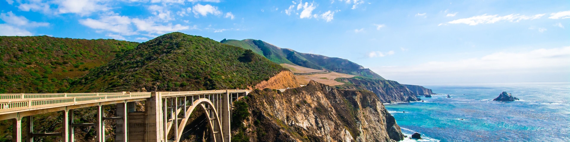 A coastal bridge with a mountainous backdrop and a beach.
