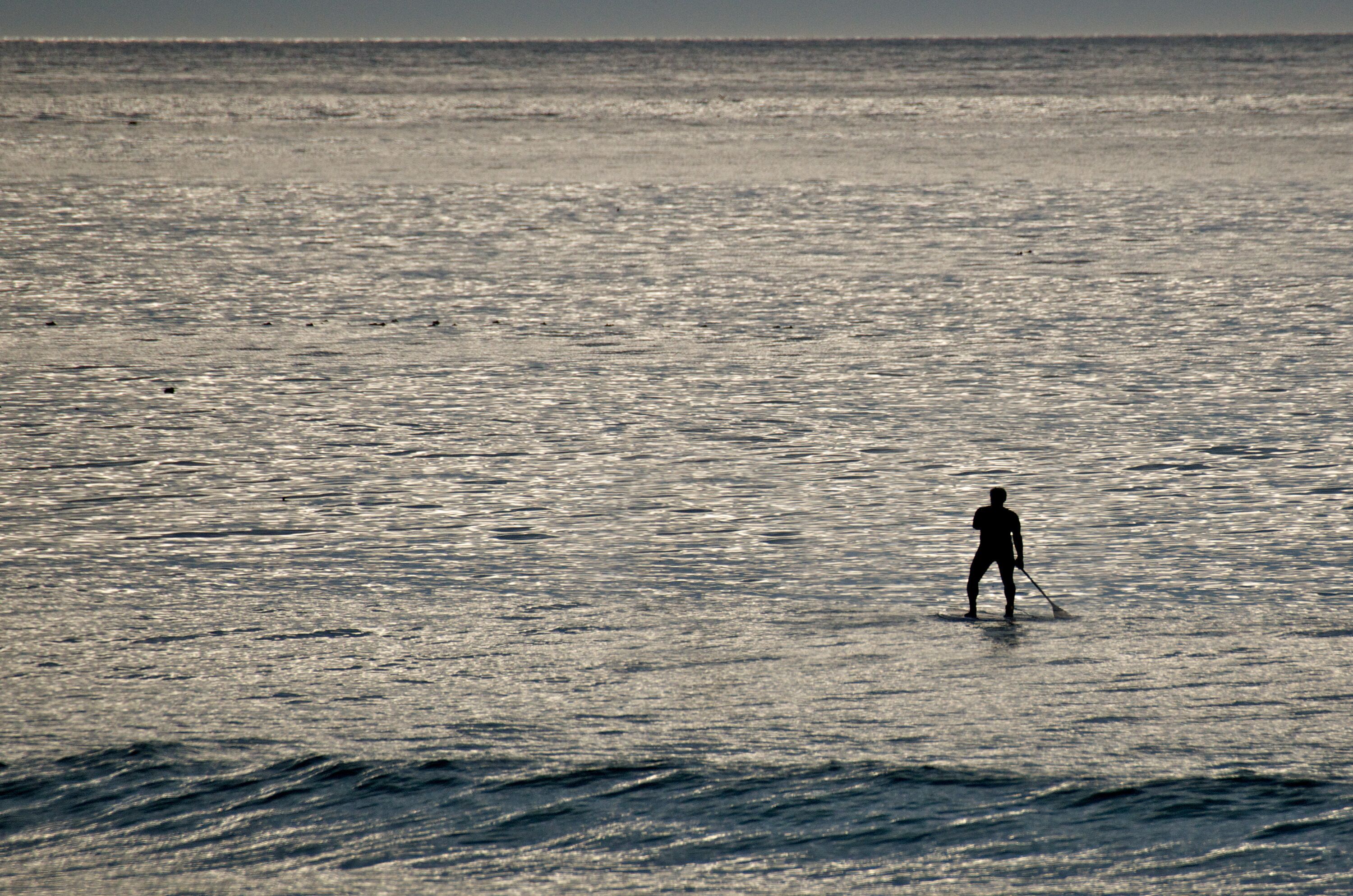 Una persona practicando paddleboard en un mar tranquilo con olas suaves.
