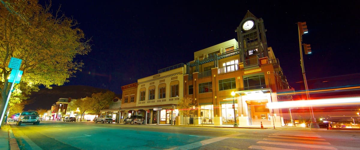 A nighttime street scene with a clock tower, lit-up buildings, and a crosswalk.